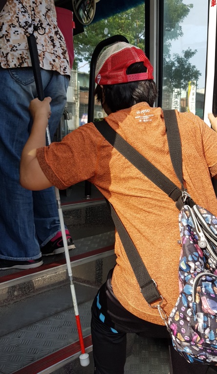 視障者在日常生活自理訓練師的指導及志工的協助下，搭乘公車前往採購地點1。