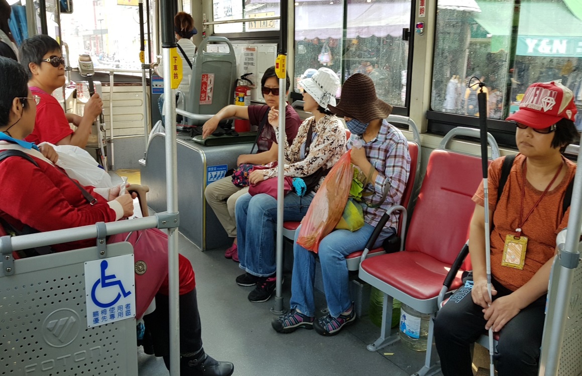 視障者在日常生活自理訓練師的指導及志工的協助下，搭乘公車前往採購地點2。