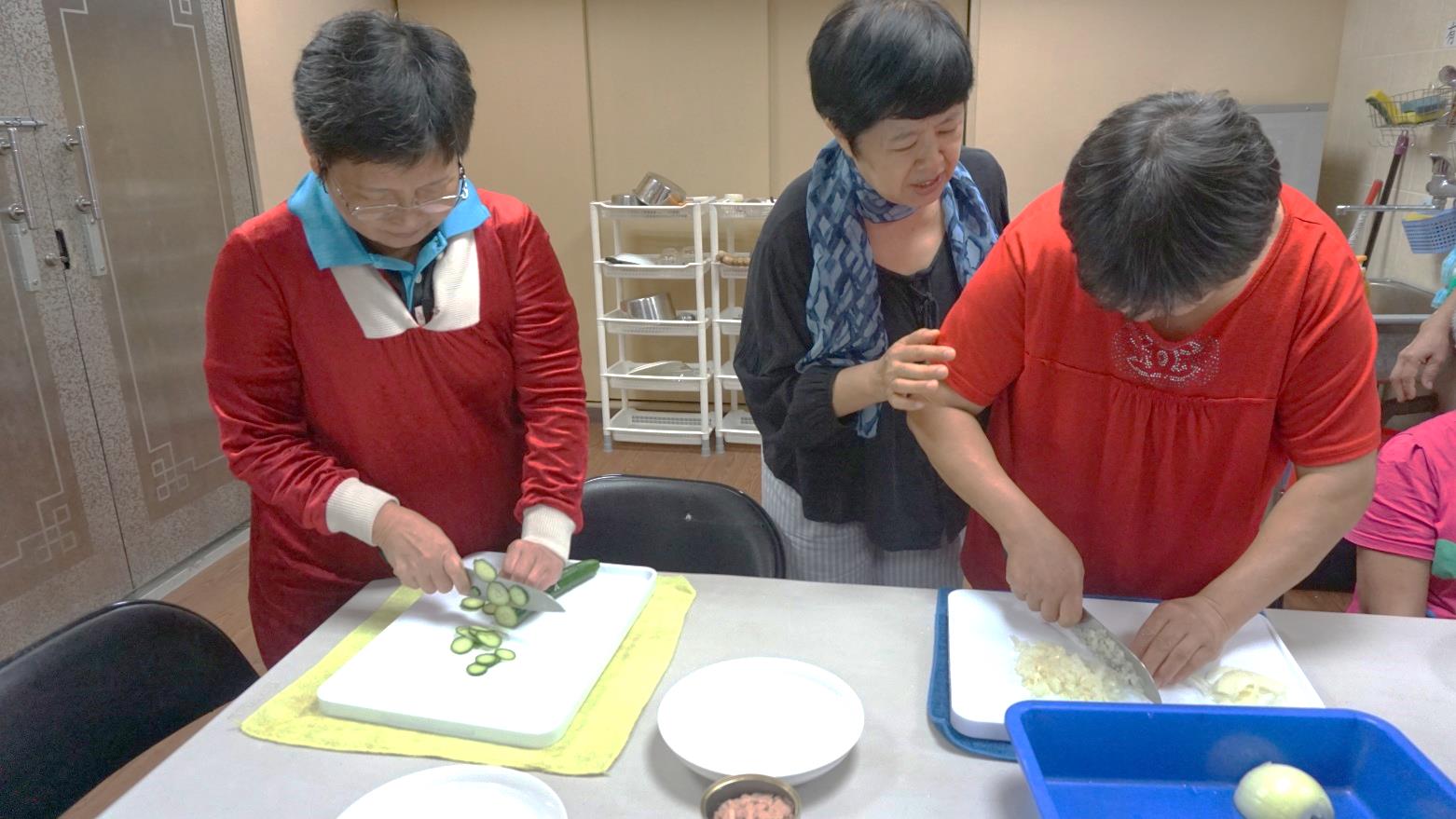 視障者透過志工在一旁的提示，調整自己切菜的手勢。
